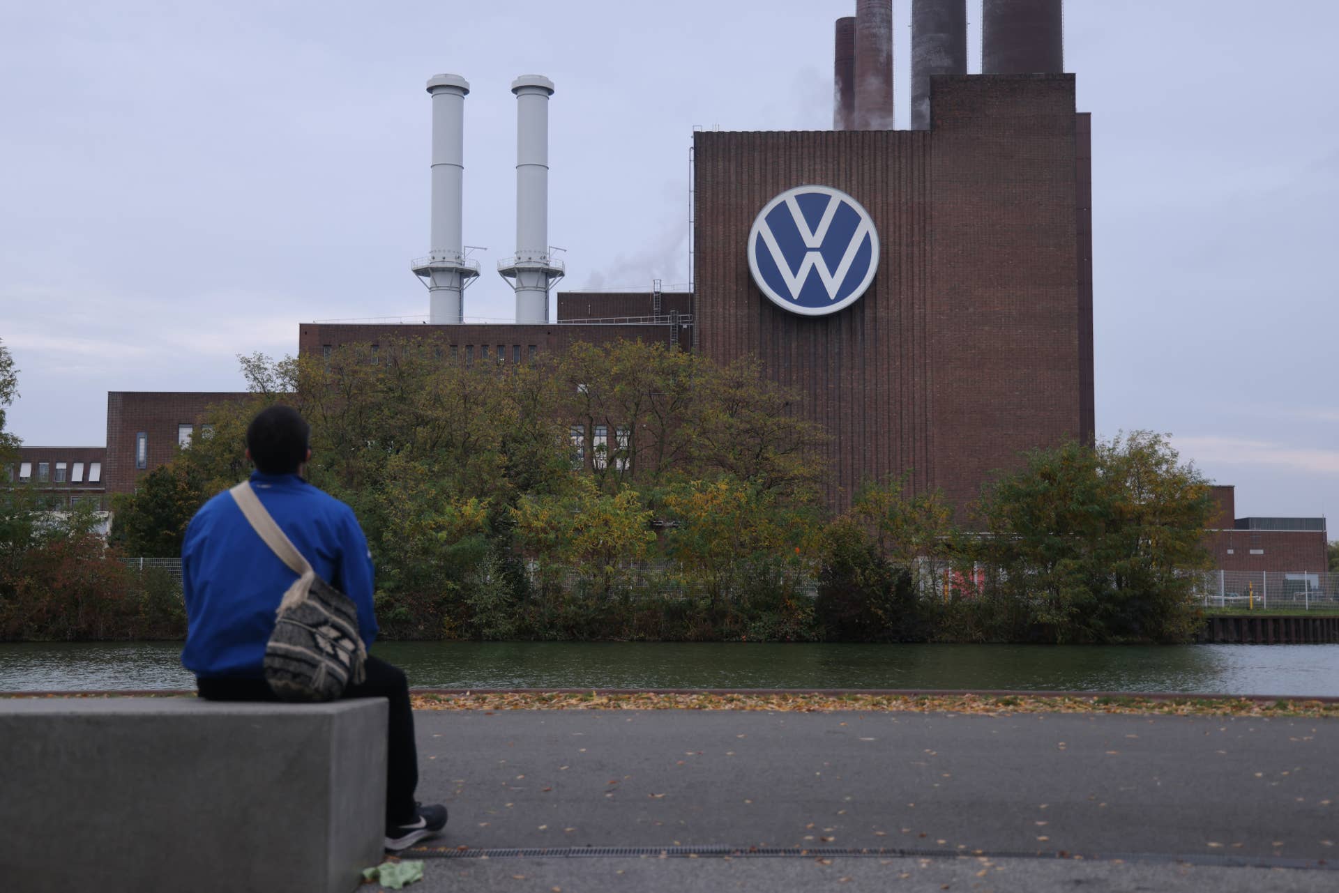 WOLFSBURG, ALEMANHA - 28 DE OUTUBRO: Um homem senta-se em frente à fábrica da Volkswagen em 28 de outubro de 2024 em Wolfsburg, Alemanha. O conselho de trabalhadores da Volkswagen anunciou hoje que a Volkswagen planeia fechar três das suas dez fábricas alemãs, num esforço para reduzir custos. A empresa viu um declínio mundial nas vendas de seus carros movidos a gasolina e elétricos. (Foto de Sean Gallup/Getty Images)
